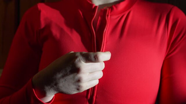 Zipper red top woman unzips a tight swimsuit to reveal cleavage in a sensual and moody indoor studio setting