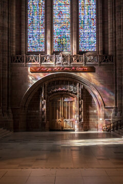 View of the interior of Liverpool Cathedral with stained glass windows and a neon art installation above a stone archway in Liverpool, England, United Kingdom.