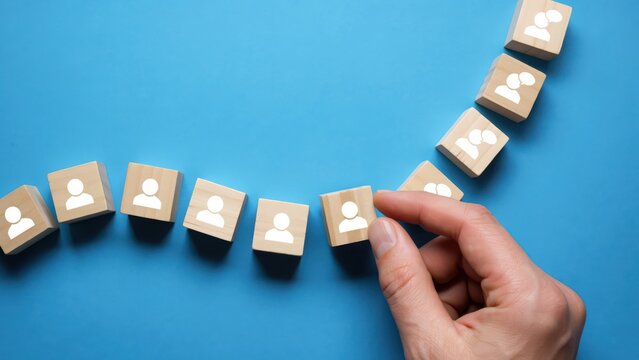 Hand placing a wooden block with a person icon onto a line of blocks, concept of team building and human resource management on blue background