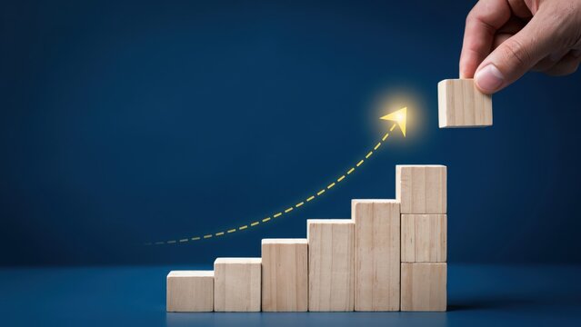 Hand placing wooden block on rising staircase with glowing arrow representing business growth and success