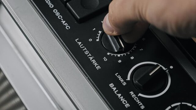 Angled close-up of a male hand turning a numbered volume dial on a classic receiver. The German Lautstarke knob adjusts sound output from zero to ten for control.