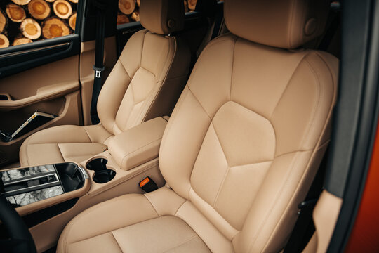 View of the front passenger and driver seats in a modern car interior with luxury beige leather upholstery. Premium vehicle cabin details showcasing elegant leather seats, armrest, and center console.