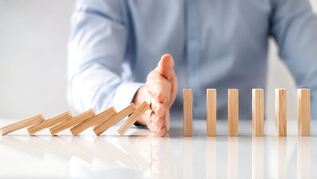 A close up of a hand preventing falling wooden blocks from creating a total collapse showcasing risk mitigation crisis control business continuity and disaster recovery