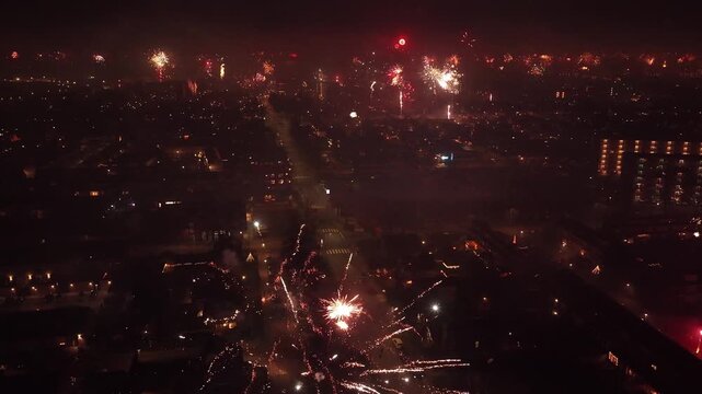 Drone descends beside an exploding firework as the entire city celebrates below.