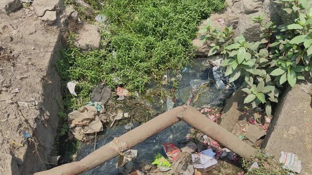 Top view of an open drainage channel carrying polluted wastewater mixed with plastic litter, packaging waste, and debris, highlighting urban sanitation challenges and environmental pollution.