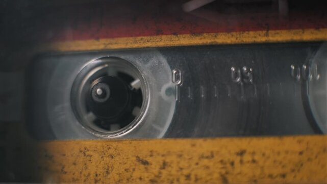 Extreme close up of a dirty yellow audio cassette tape playing inside a deck mechanism. The rotating spindle hub moves continuously. Concept of retro music and analog technology nostalgia.
