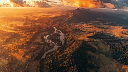 Obraz premium Aerial drone view of a winding river flowing through a vast mountain valley at sunset with clouds