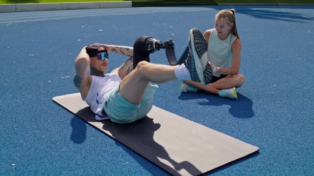 Man with prosthetic leg does knee to elbow crunches with trainer