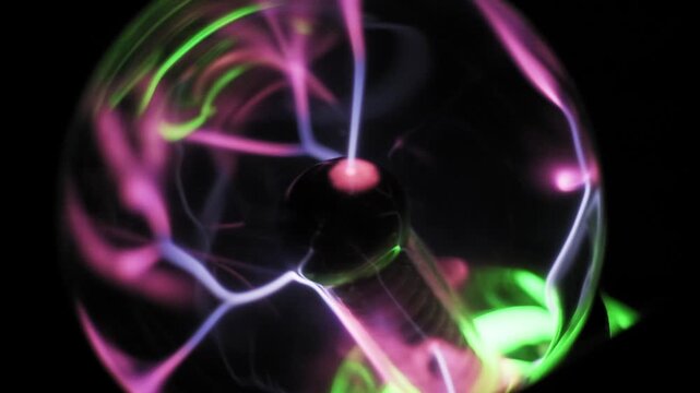 Angled view of a plasma globe where electric bolts emanate from the central electrode. Pink, white, and purple streams swirl inside a glass sphere with green light accents.