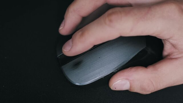 Top-down view of a male hand clicking a black computer mouse on a dark textured pad. The fast action highlights professional gaming, esports competition and intensive digital workflow.