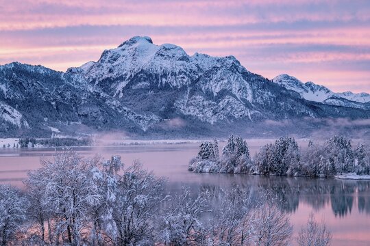 Dawn and sunrise at the wintry Forggensee in a snow-covered winter landscape in the foothills of the Alps in the Allg&auml;u in Bavaria, Germany