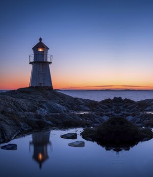 Lighthouse surrounded by rocks at night, lighthouse with lights on at sunset