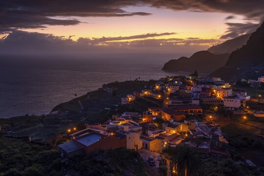 The village of Agulo shortly in front of sunrise. Houses and streets are still illuminated. View of the sea and the coast. Agulo, La Gomera, Canary Islands, Spain