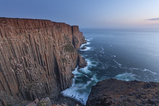 At The Gap, long exposure shows sunset over the cliffs of Cape Raoul. Golden light hits the sea and colors the rocks warmly in the evening. Cape Raoul, Tasman Peninsula, Tasmania, Australia