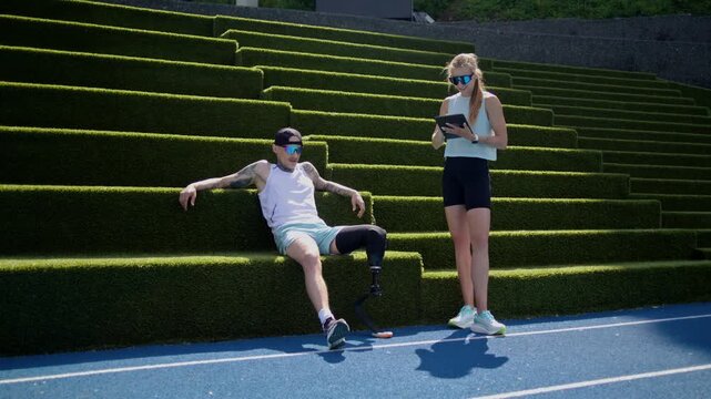 Instructor holds tablet as runner with bionic leg prosthesis sits