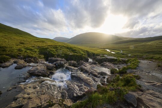 River flows through green hills in sunset light under a cloudy sky, Fairy Pools, Grula, Isle of Skye, Scotland, United Kingdom, Great Britain