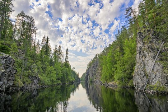 A calm lake lies in a wooded gorge, surrounded by tall rocks and reflecting the sky covered with clouds Julma-&Ouml;lkky Canyon Gorge, Hossa National Park, Irni, Northern Ostrobothnia, Finland