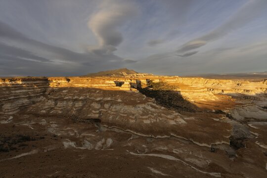 Eroded sedimentary rock formations with layered rock structures in evening light, mountain and clouds in the background, steppe landscape of Patagonia, Santa Cruz province, Argentina