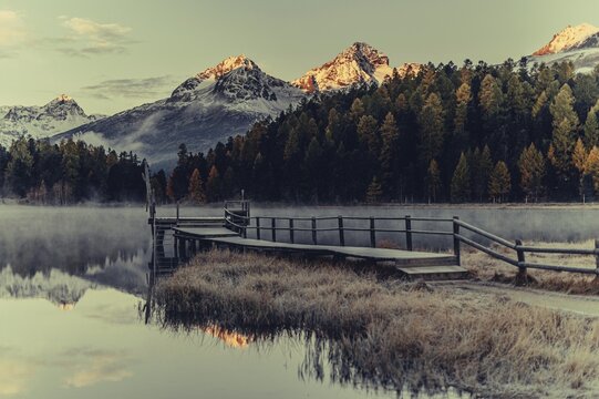 Lake Staz near Sankt Moritz in the Engadin in Switzerland. Morning atmosphere with fog in autumn. Water reflection and snow-covered mountains in the background