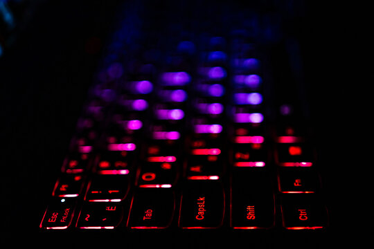Low key macro of a backlit laptop keyboard reveals rows of violet and magenta lights with red accents. Smooth bokeh and gentle depth produce a rich abstract look for futuristic branding.