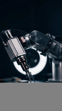 Precision robotic arm handling microchip on circuit board under ring light in dark lab