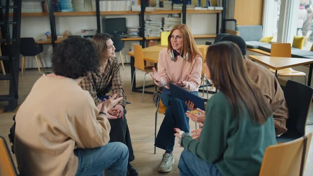 Group of students discussing ideas in a library setting during the day while sitting on chairs and sharing thoughts with each other