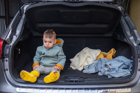 Toddler Sitting in Open Car Trunk in Garage.