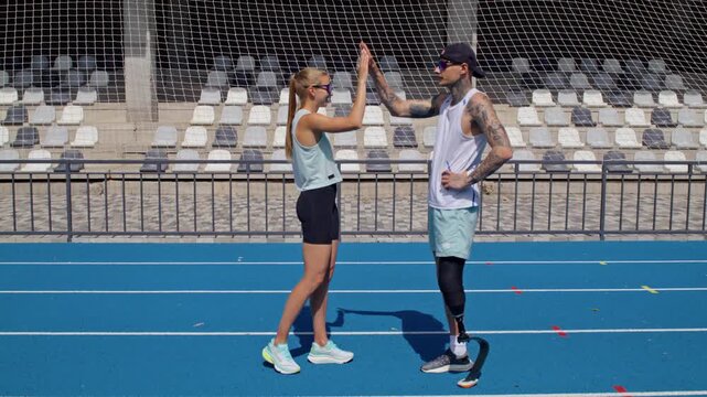Runner with bionic leg prosthesis gives high five to instructor
