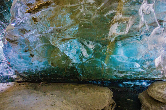 View of the translucent blue ice formations inside a glacier cave with sediment streaks and a rocky floor in Arandu, Khyber Pakhtunkhwa, Pakistan.