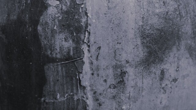 Black and white abstract close-up of stained wall corner with peeling material, rough patches, dust marks, and dramatic grunge contrast.