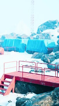 Workers are preparing a construction area on ice. A red platform is in front, and large rocks surround the site. Blue tarps cover some materials for protection. Snow is on the ground.