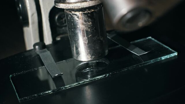 A pipette drops a clear liquid sample onto a glass microscope slide under the lens. This macro shot highlights scientific research and precise laboratory analysis.