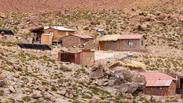 View of small stone and wooden houses equipped with solar panels and modular heating panels on a rocky hillside in Machuca, Antofagasta, Chile.