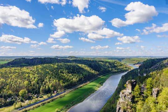 Stunning aerial view of Elbe river canyon and basti sandstone rocks in Saxon Switzerland, beautiful spring landscape with a train traveling along the valley under a blue sky, Saxony, Germany.