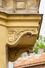 Detailed view of ornate architectural corbels supporting a balcony on a historic yellow building facade showing classical decorative relief carvings © K