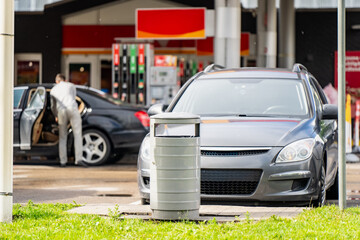 Front view of a gray family car parked next to a trash bin at a petrol station forecourt, representing fuel stop and automotive travel © K