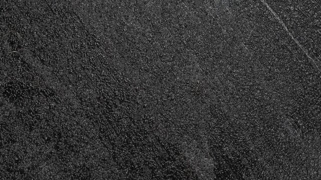 Dark textured surface with fine granular patterns, subtle streaks, and rough matte appearance. Grunge texture background animation.