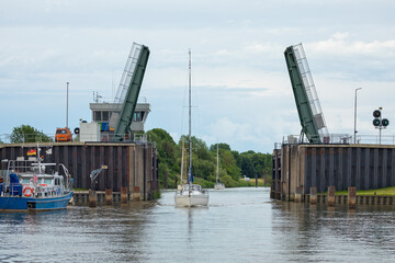Obraz premium Sailboats pass through a floodgate with a bascule bridge on the River Schwinge at Stade