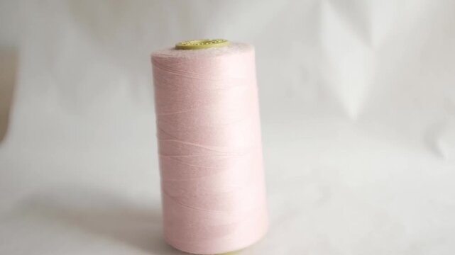 Studio shot of a large spool of pastel pink sewing thread standing upright. Soft and even lighting,  minimalist aesthetic. Sewing, tailoring, fashion design, textile industries, handmade crafts, DIY