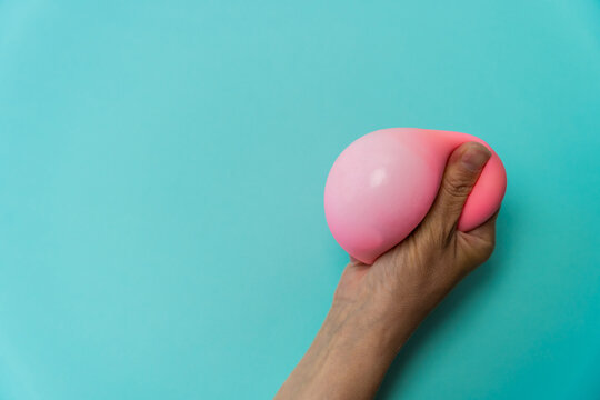 Hand squeezing a pink anti-stress dumpling toy against a light blue background, showcasing the toy's soft texture and flexible shape in a close-up view