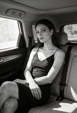 Elegante junge Frau im schwarzen Kleid auf der R&uuml;ckbank eines Autos &ndash; Schwarz-Wei&szlig;-Portr&auml;t