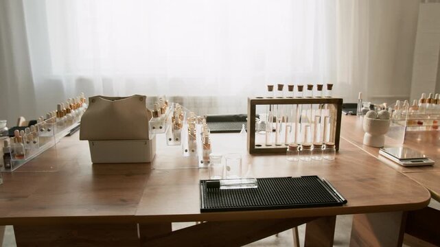 Perfume masterclass workstation featuring dropper bottles and test tubes on wooden table, camera panning. Suitable for promoting cosmetics branding, aromatherapy courses, or fragrance workshops