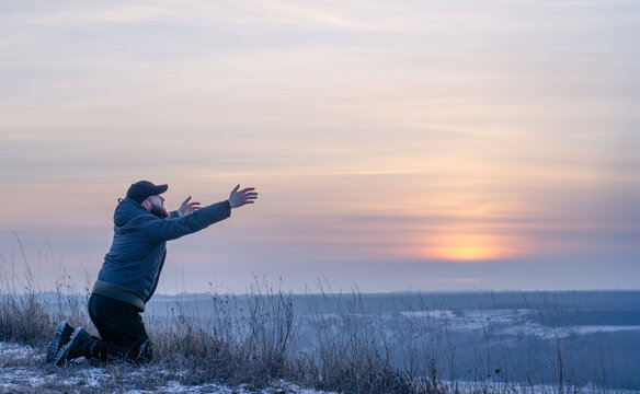 A man kneels in prayer to God with his hands outstretched to the sky. Praying with faith