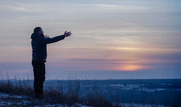 A man kneels in prayer to God with his hands outstretched to the sky. Praying with faith