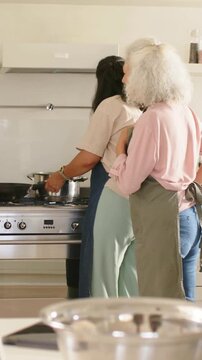 Vertical video: Pouring oil, cook in blue apron stirring pan on range, partner aiding meal prep
