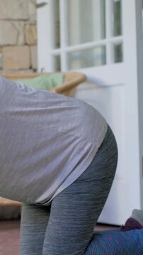 Vertical video: Starting kneeling, woman in workout gear pulling purple dumbbell on porch, tracker