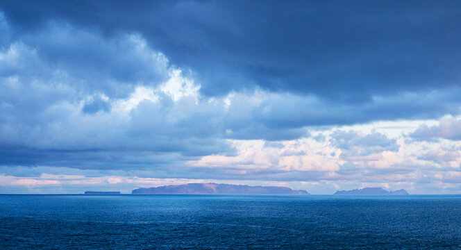 Wide panoramic view of the distant Desertas Islands silhouette on the ocean horizon under sunset clouds from Canico coast, Madeira, Portugal.