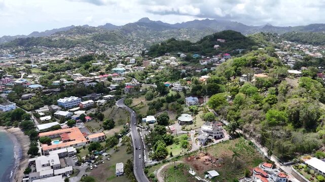 aerial above ush green tropical hillside neighborhoods and dense residential communities bordering the coastal waters of Saint Vincent island.