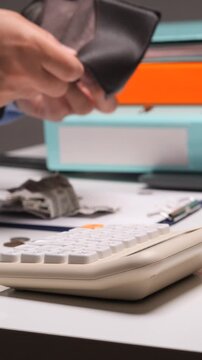 Vertical video person's hands opening an empty wallet above a desk with scattered cash, coins, and a calculator, illustrating budget constraints, debt, and the need for financial planning