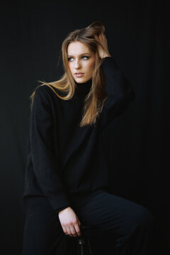 Captivating portrait of a young woman wearing a black sweater, with tousled hair and an intense gaze. The soft lighting and dark background emphasize her natural beauty and elegance